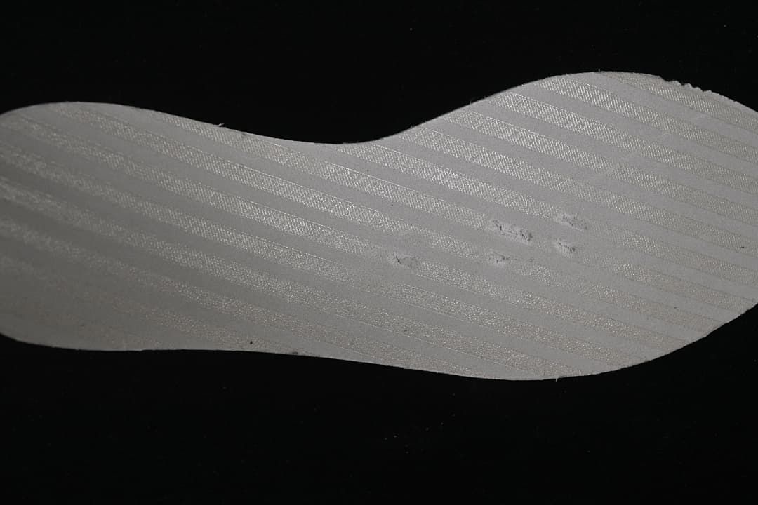 Close-up of a pale shoe component against a dark background.
