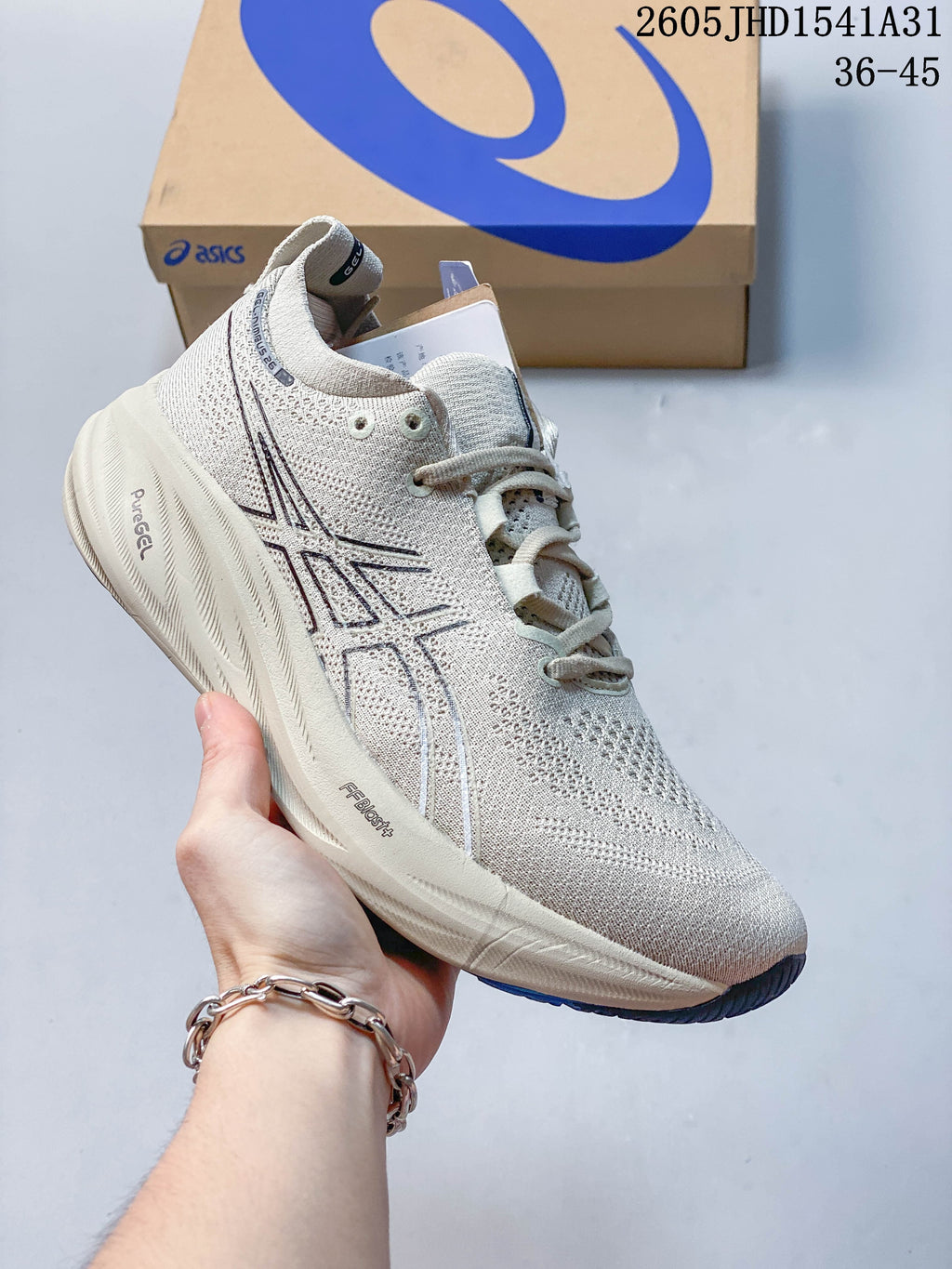 Light gray ASICS GEL-NIMBUS 26 running shoe with dark accents, shown in front of an ASICS shoe box.