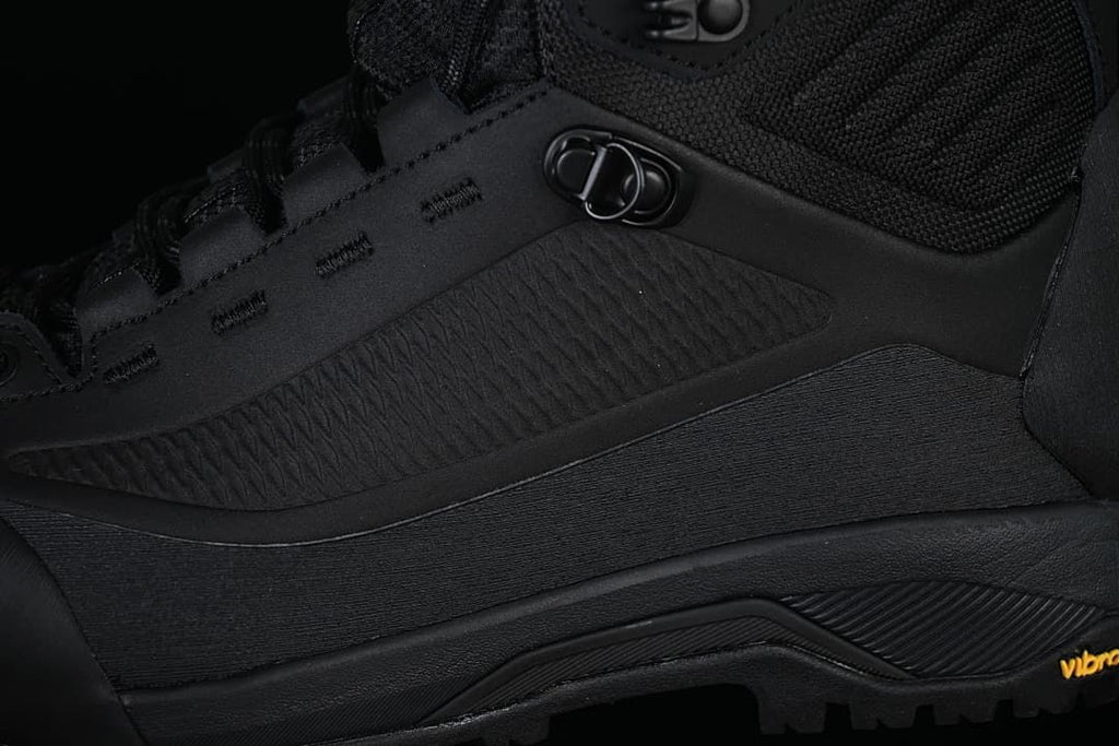 Close-up of the black boot's side panels, lace hardware and outsole.