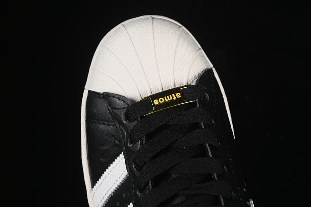 Top-down close-up of the shell toe and black laces with a gold-tone lace detail