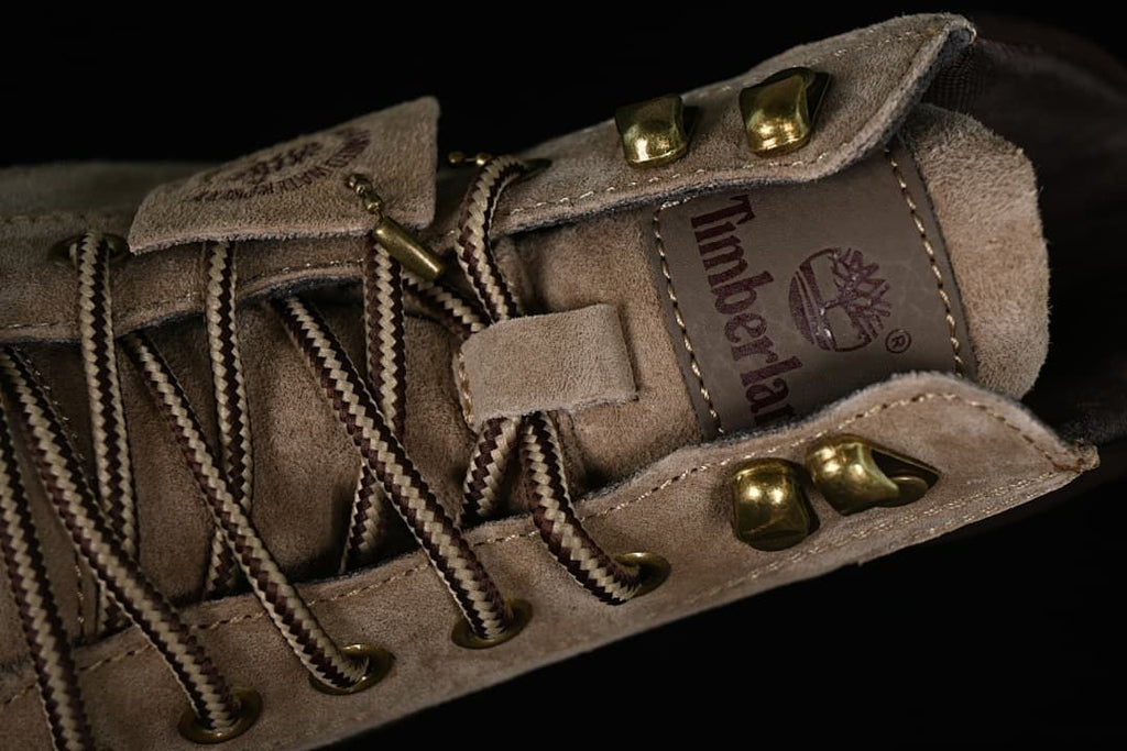 Close-up of the lacing system with brown-and-cream laces, metal hooks, and a branded tongue patch.