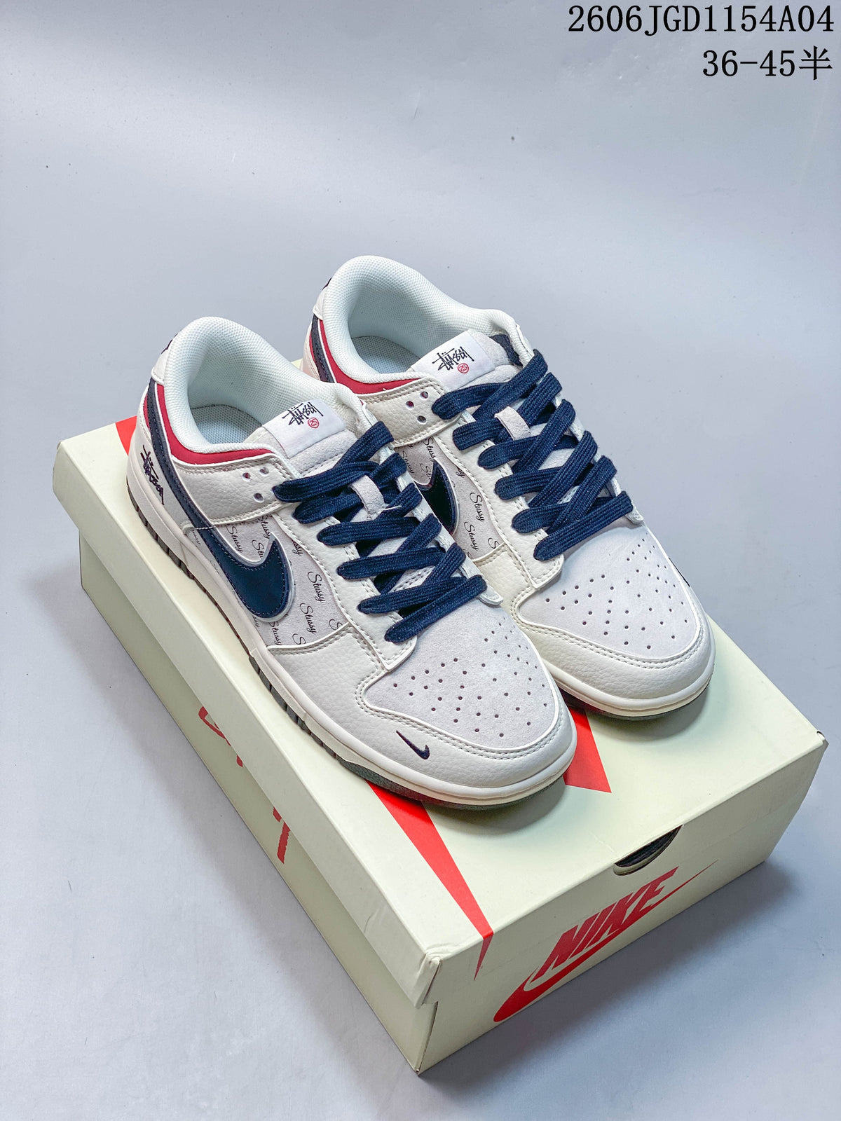 Pair of light-colored Nike SB Dunk Low sneakers with navy laces, navy Swooshes, red heel accents, and a shoe box.