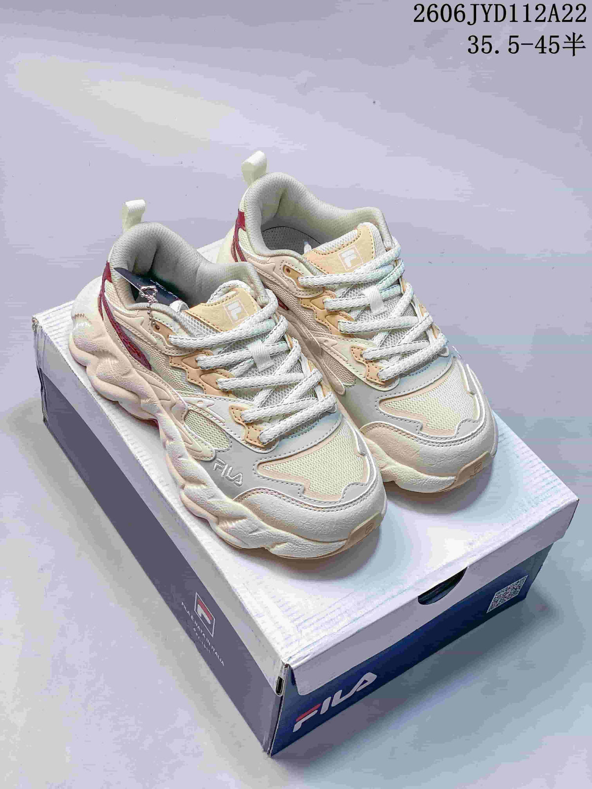 Pair of cream and beige FILA sneakers with burgundy accents and chunky sculpted soles, shown on a shoebox.
