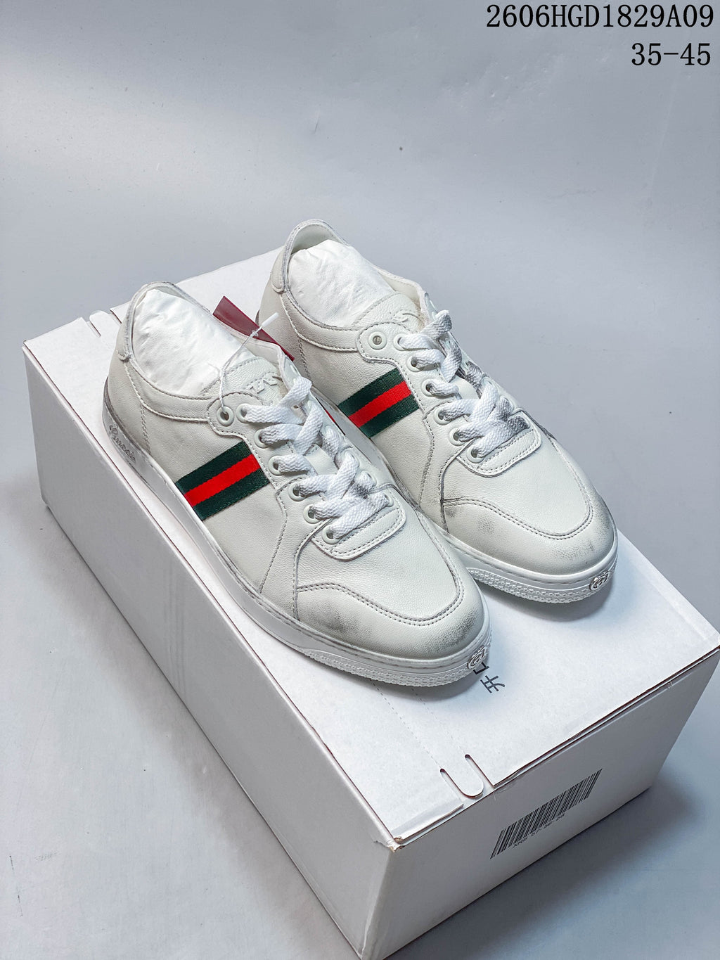 Pair of white low-top sneakers with red-and-green side stripes, shown on a box.