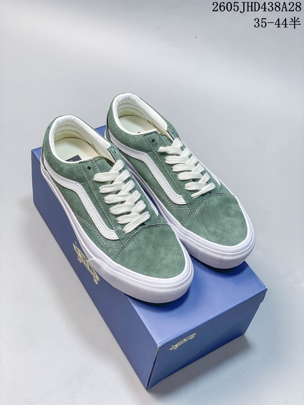 Pair of green low-top sneakers with white side stripes and laces, displayed on a blue shoe box.