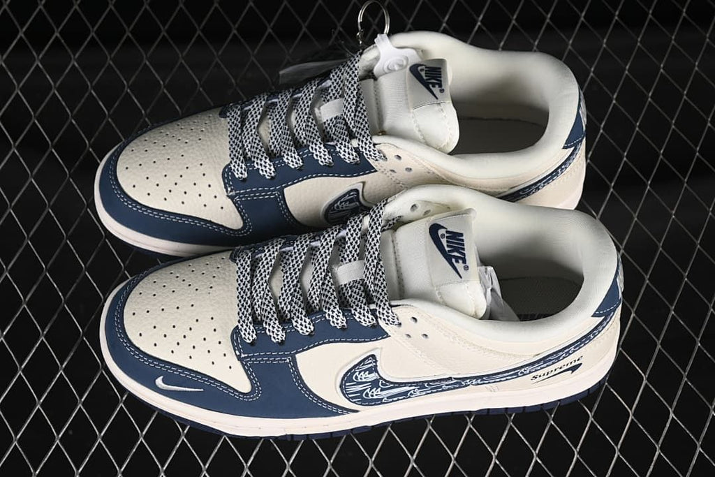Top view of a pair of cream and navy low-top sneakers with patterned laces and perforated toe panels.
