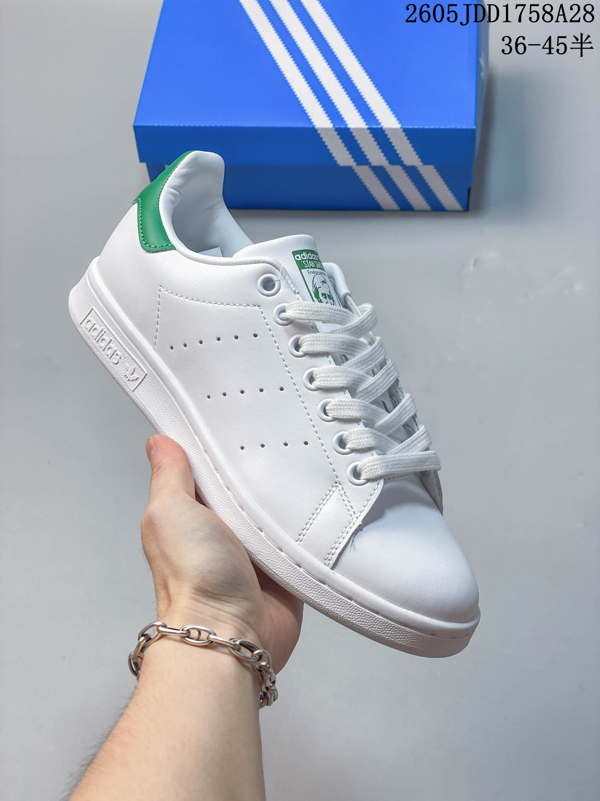 Angled side view of a white Adidas sneaker with green heel accent