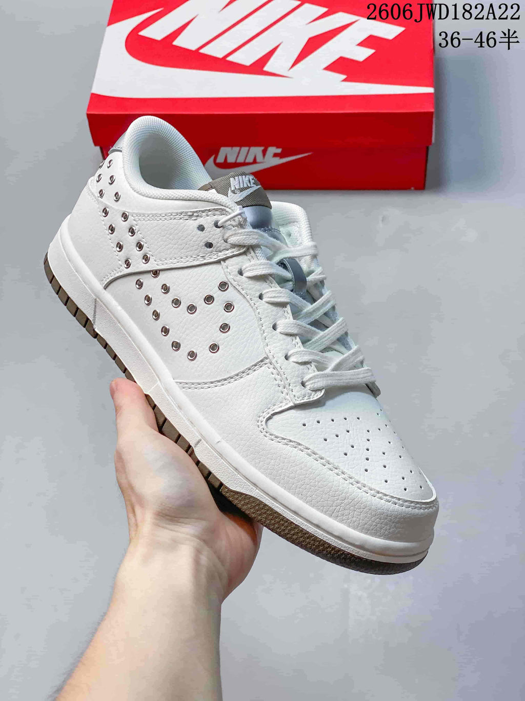 Angled view of a white low-top sneaker with silver-tone studs and a perforated toe