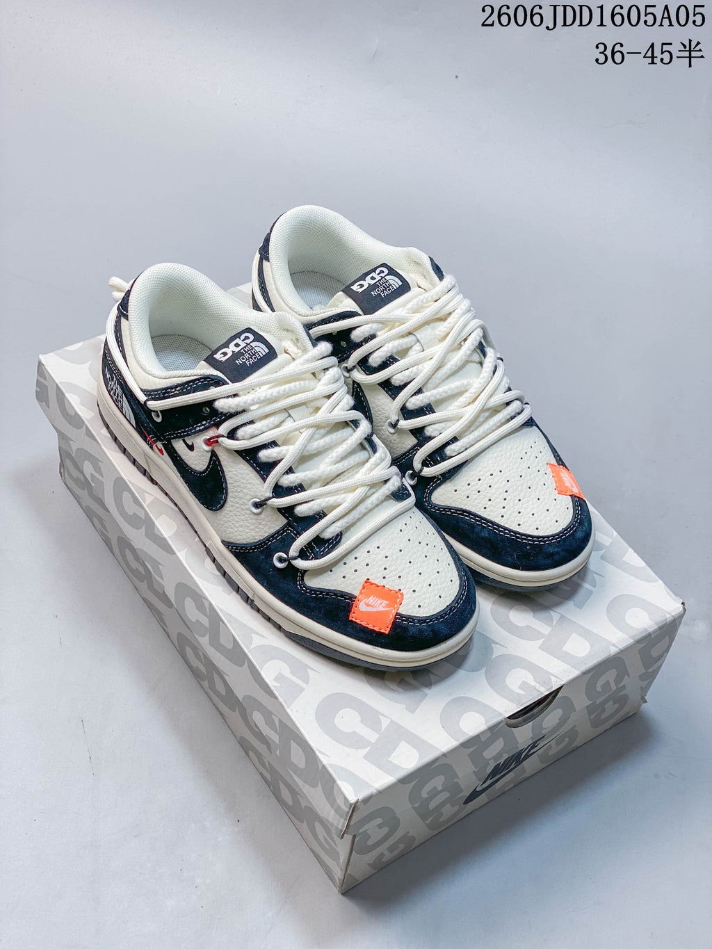 Pair of off-white and navy Nike SB Dunk Low sneakers with orange accents on a patterned box