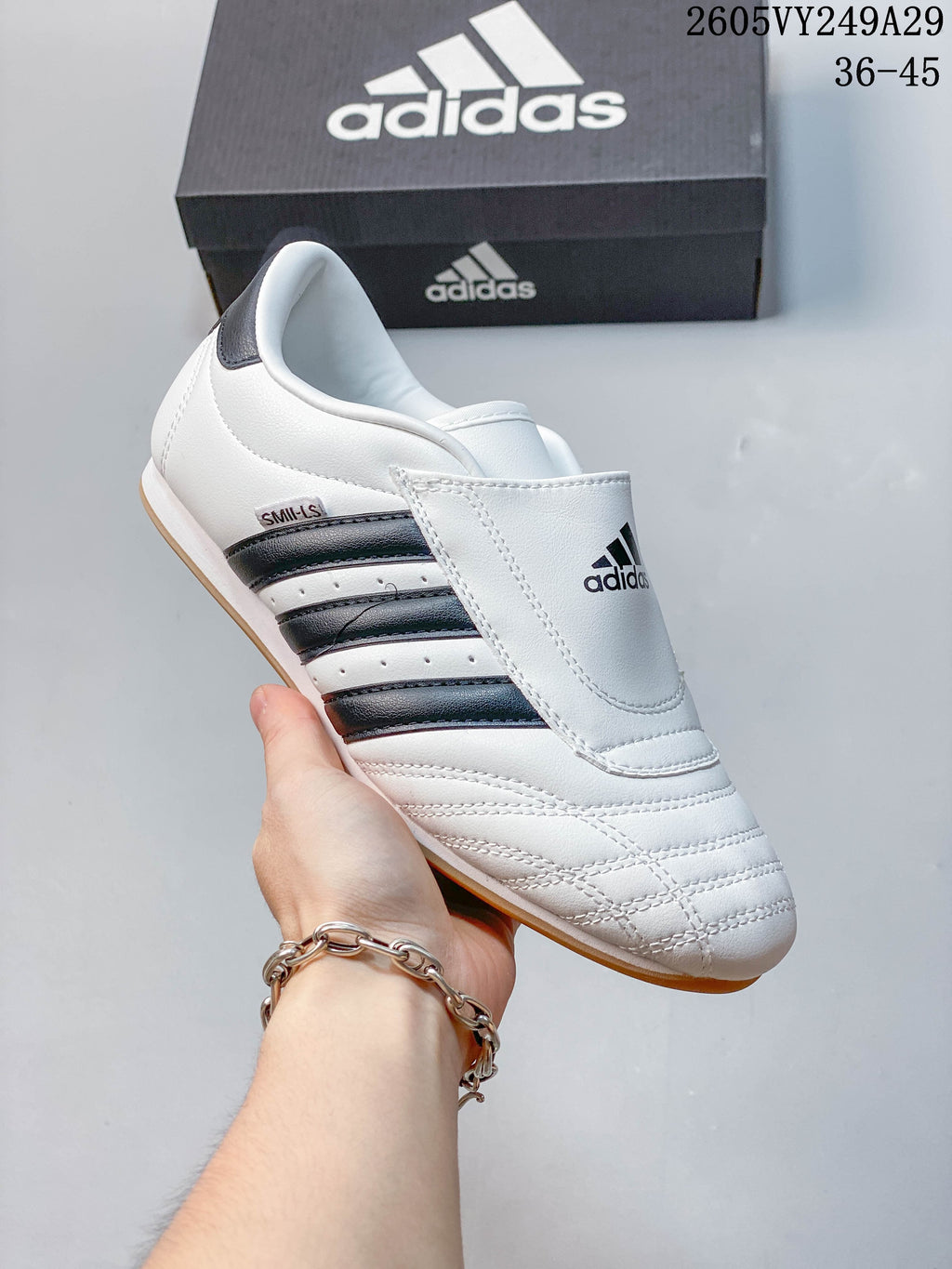 Close-up of a white low-top shoe with a broad instep strap, dark side stripes and a light brown-toned outsole.