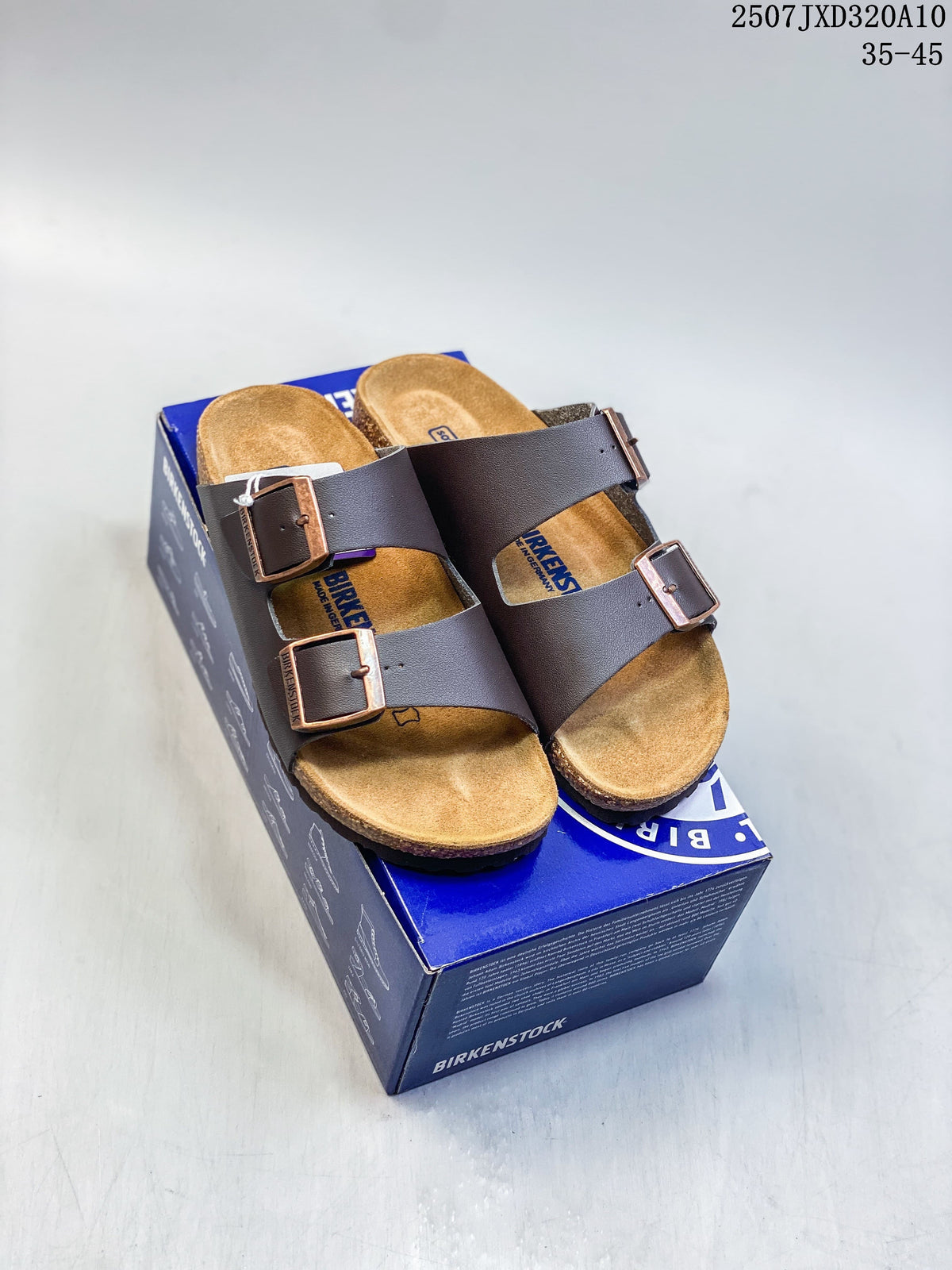 Dark brown two-strap slide sandals with metal-tone buckles displayed on a blue shoebox
