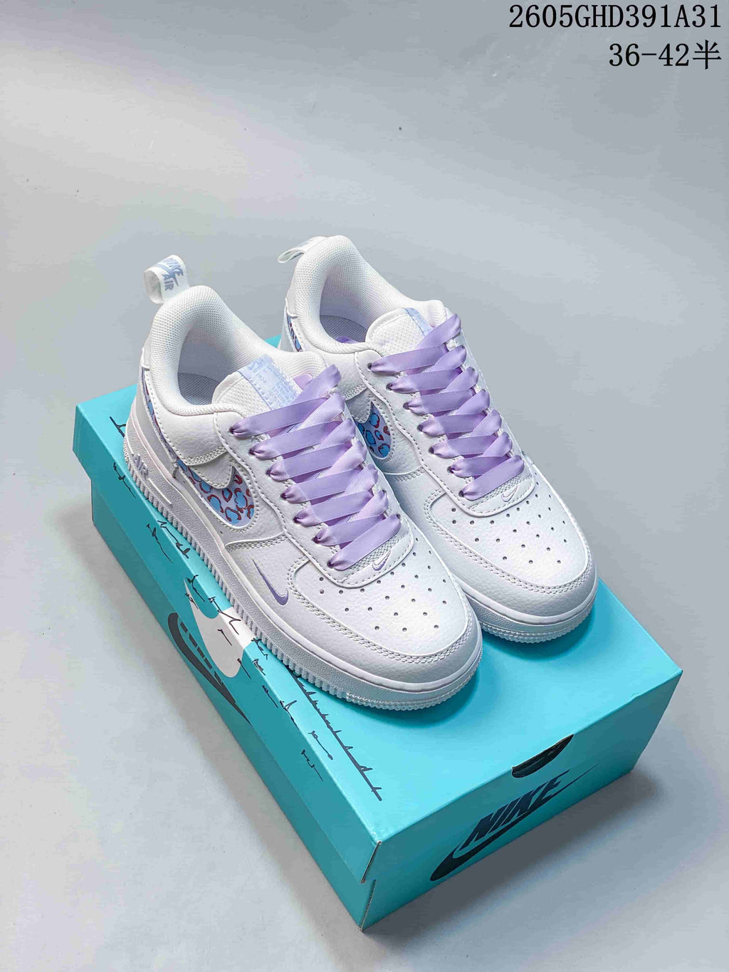 Pair of white Nike Air Force 1 Low sneakers with lavender laces and patterned side panels on a turquoise shoebox