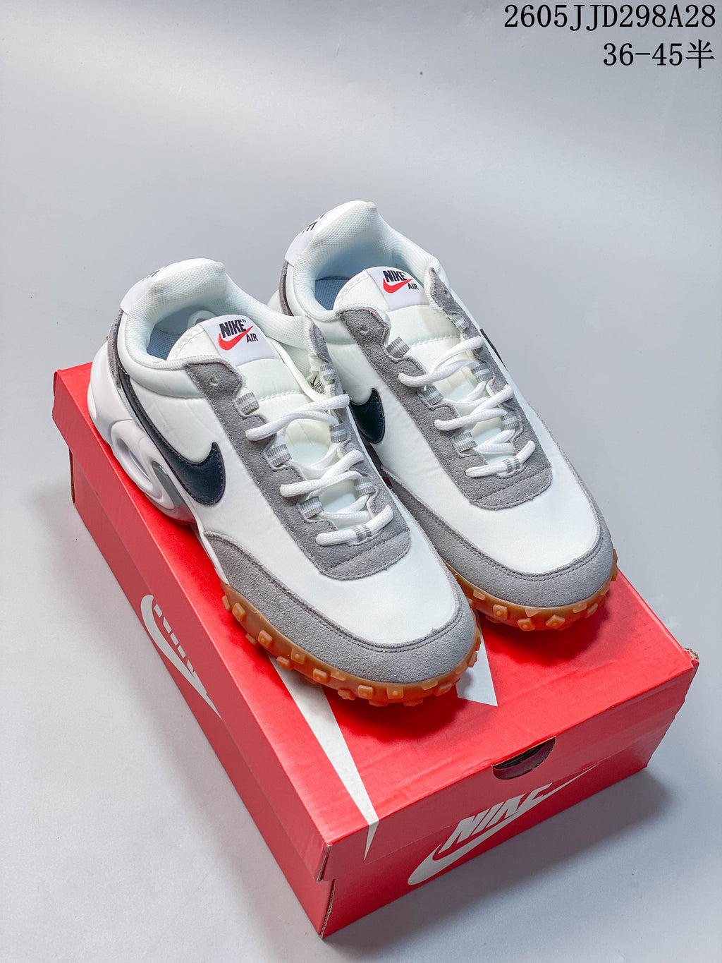 Pair of white and grey Nike Air Max Waffle SP sneakers with dark Swoosh accents and gum outsoles, shown on a red shoebox.