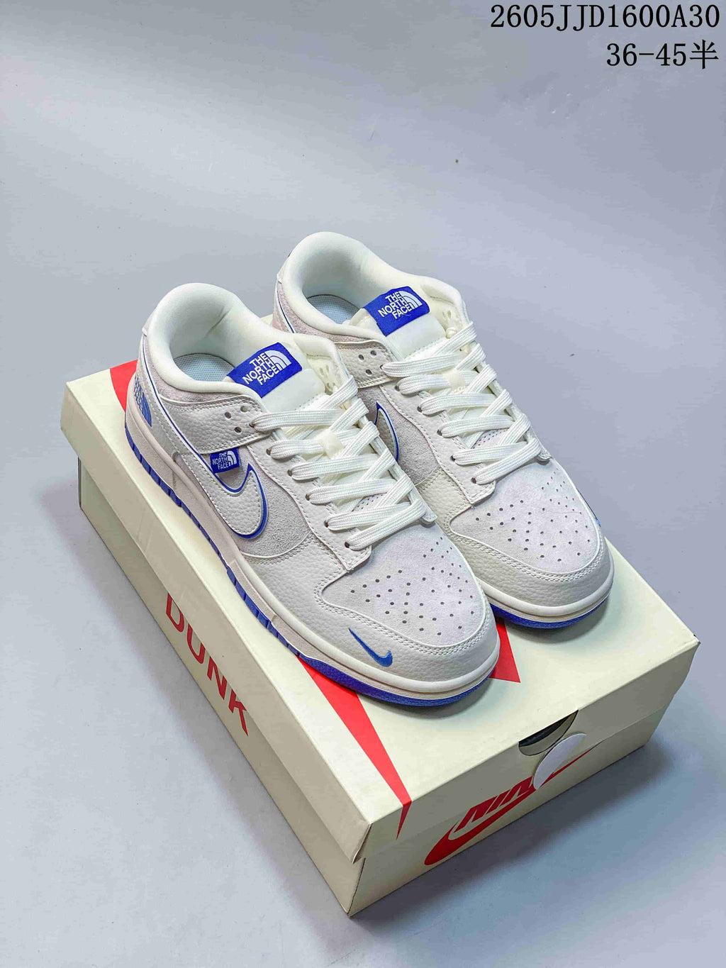 White and light gray Nike SB Dunk Low sneakers with blue accents, shown on a shoe box
