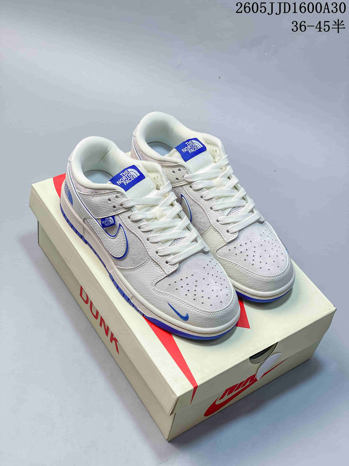 White and light gray Nike SB Dunk Low sneakers with blue accents, shown on a shoe box