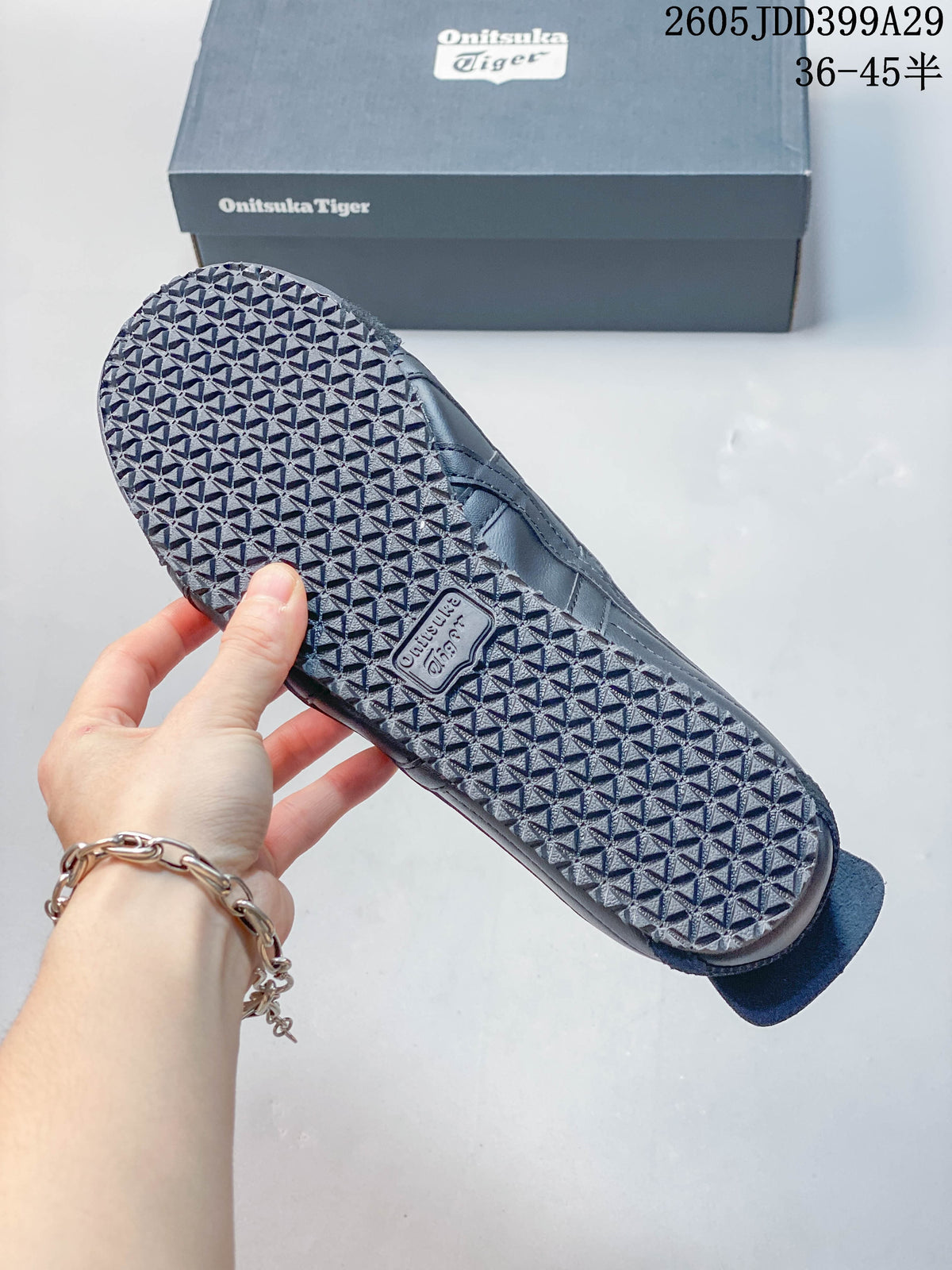 Close view of the patterned outsole of a gray Onitsuka Tiger sneaker, with a branded shoe box in the background.