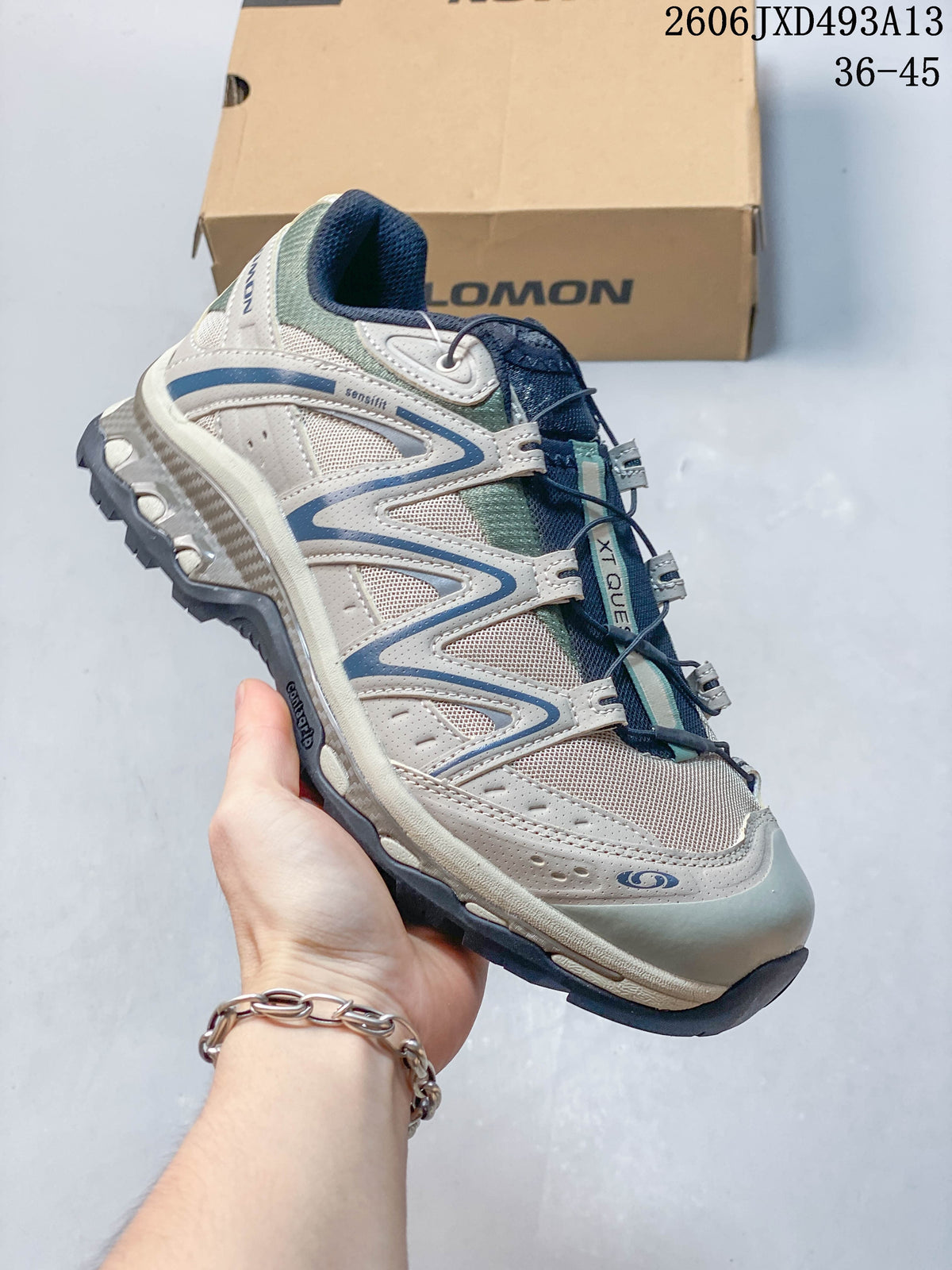 Angled side view of a sand-gray Salomon shoe with pale green and navy accents.