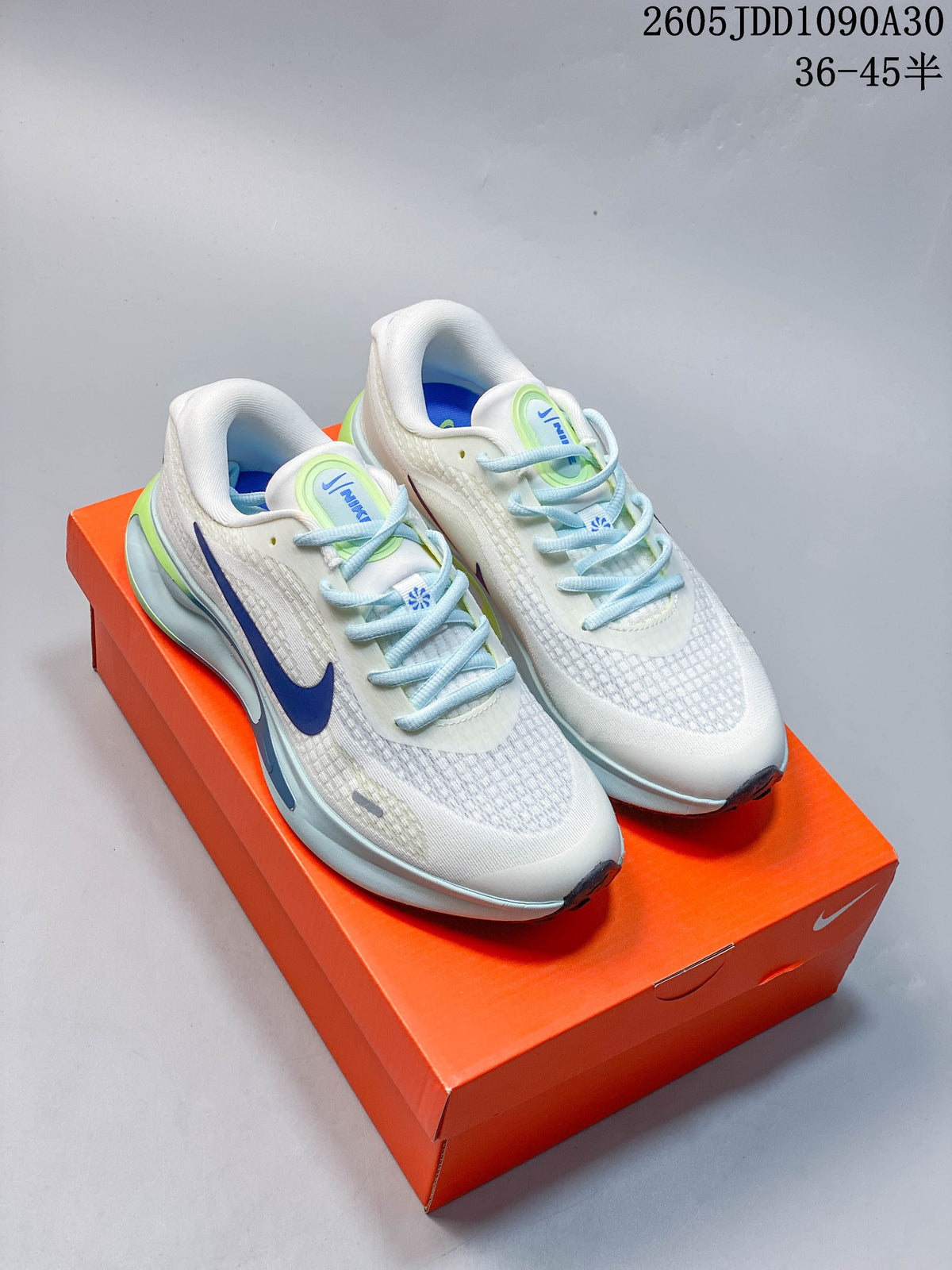Pair of white Nike Journey Run shoes with blue and lime accents, shown on an orange shoe box.