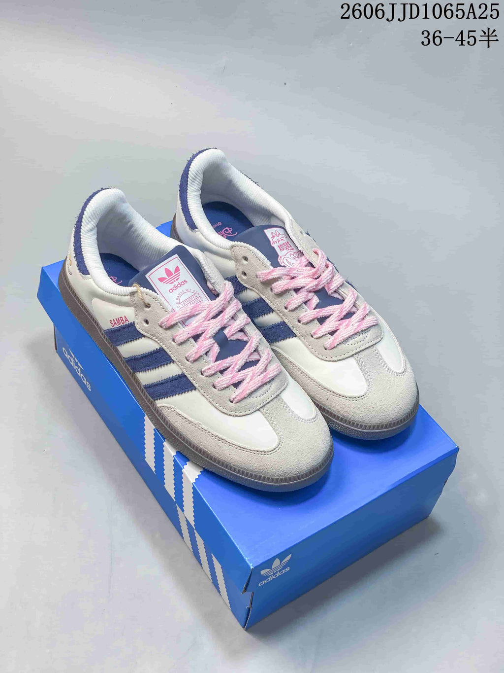 White low-top sneakers with blue stripes, pink laces, and gray-toned outsoles on a blue shoebox