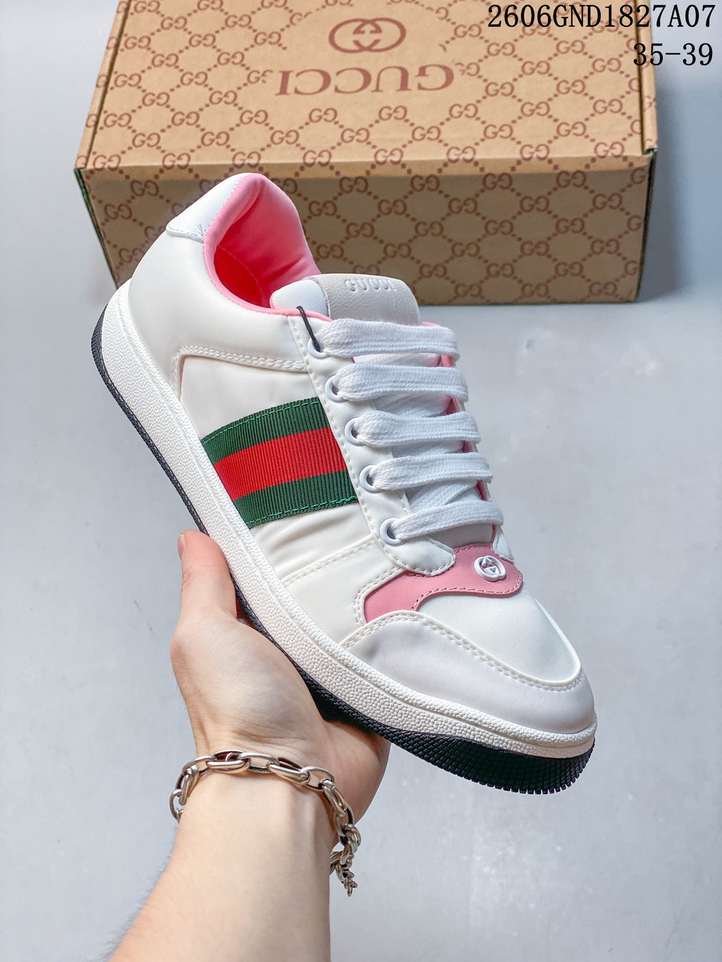 Angled side view of a white low-top sneaker with pink details and a green-and-red stripe.