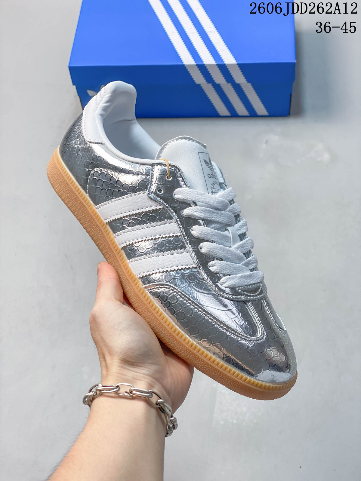 Close-up of a reflective silver low-top sneaker with a textured finish, white stripes, and gum-colored sole.