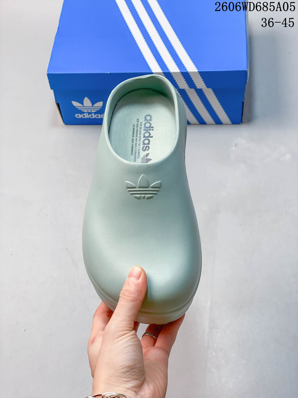 Top view of a light blue mule shoe with a closed toe and Trefoil logo