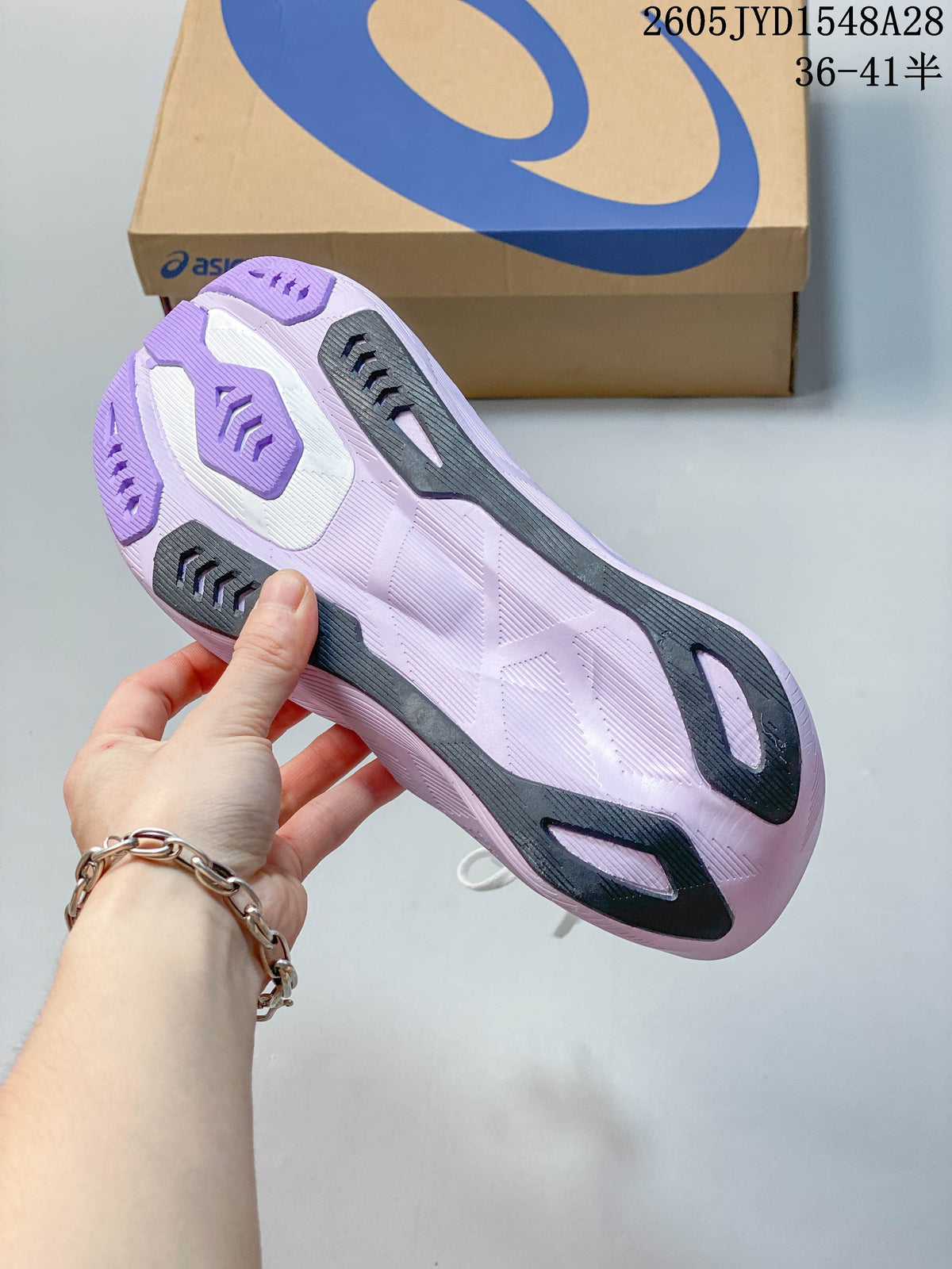 Underside of a white and purple running shoe showing its patterned outsole