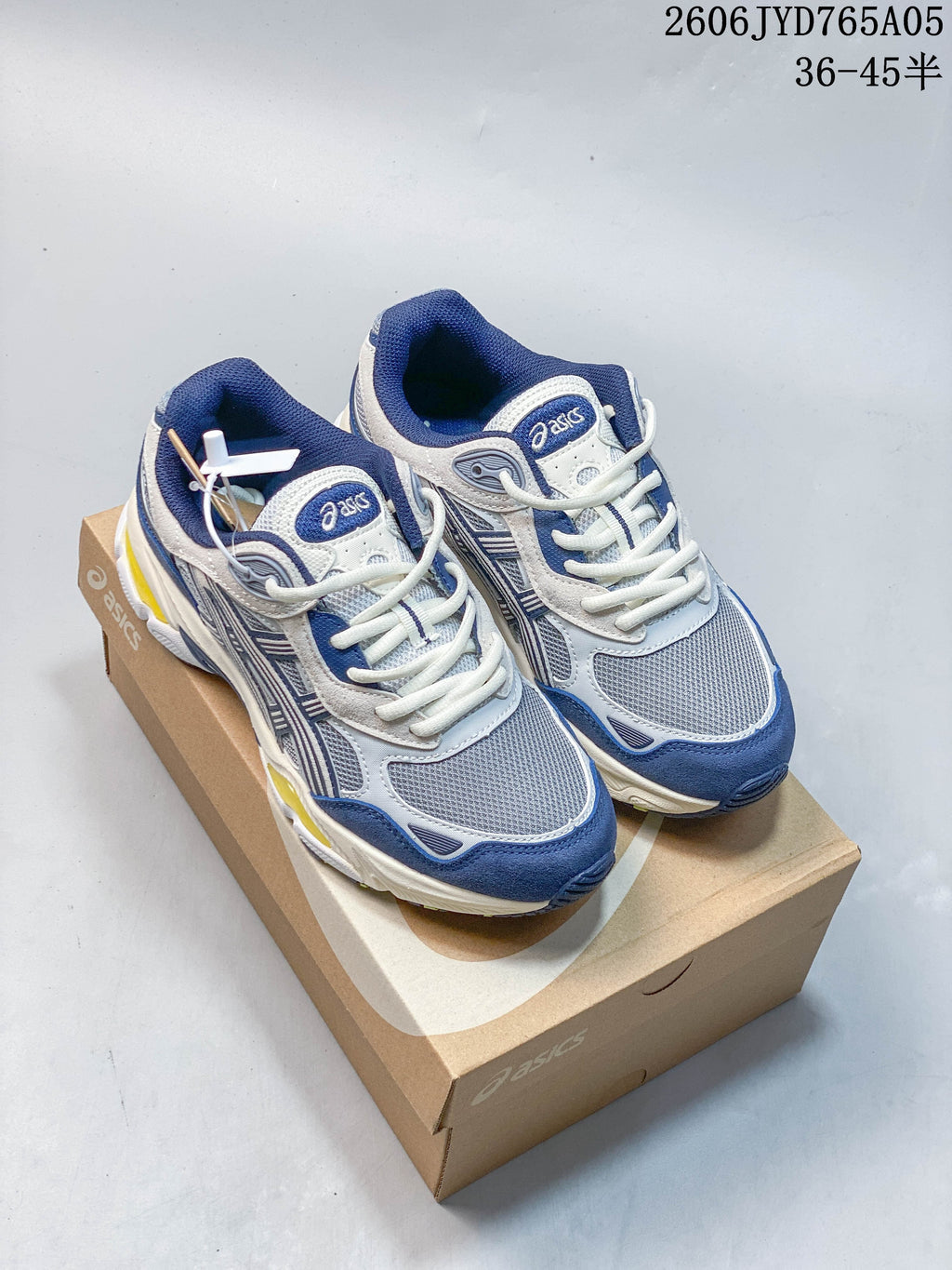 Blue, white and gray ASICS sneakers with yellow midsole accents, shown on a shoebox; image also displays a size range.
