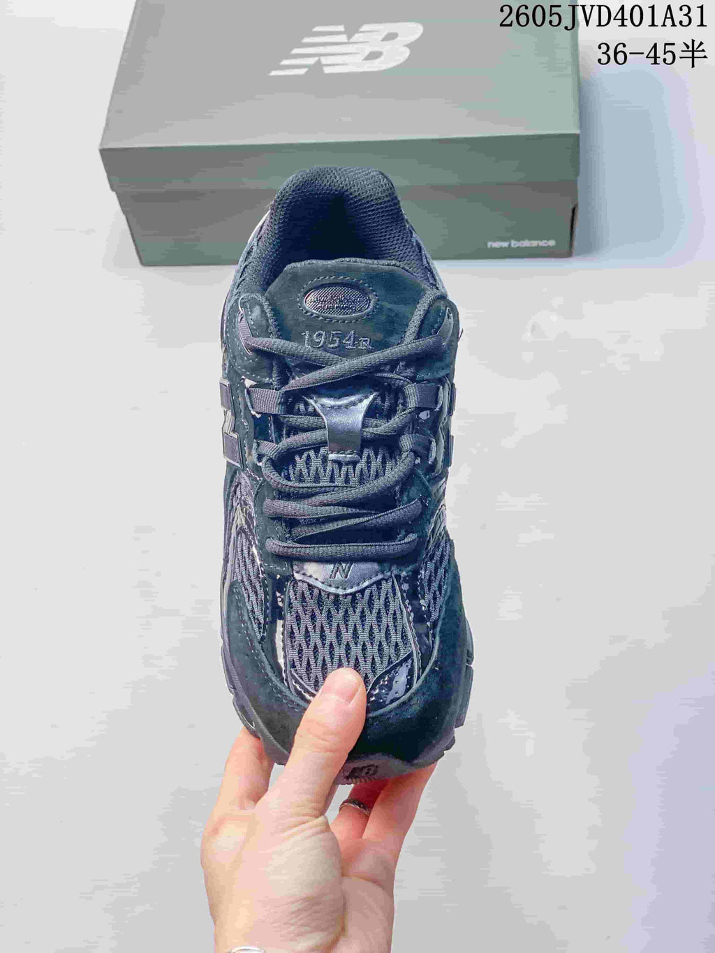 Top view of a charcoal gray New Balance sneaker with lace-up closure and 1954 tongue branding; size range text appears in the image.