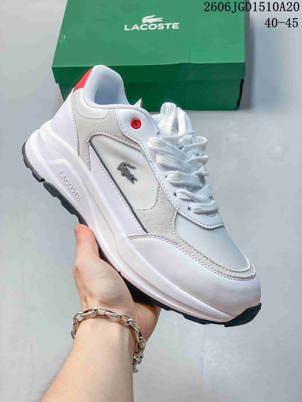 White Lacoste low-top sneaker with light gray panels and a red eyelet accent