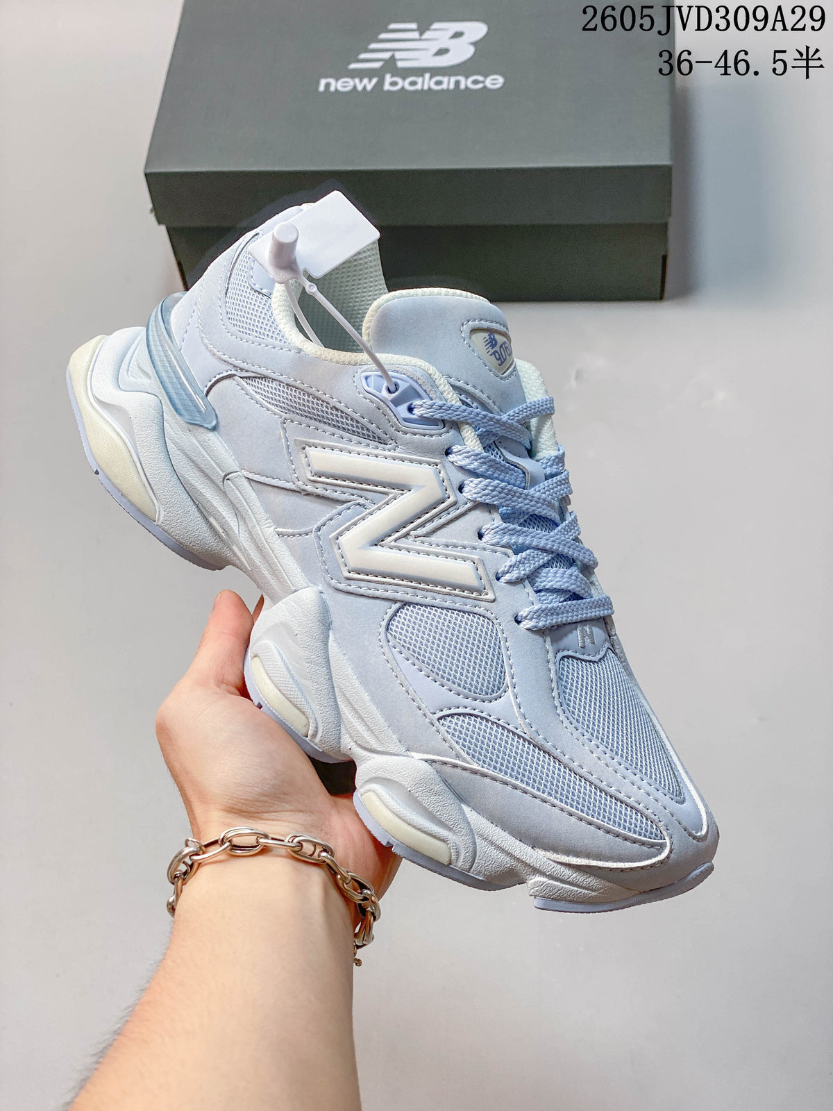 Angled side view of a pale blue and white New Balance 9060 sneaker with layered panels and a chunky sole.