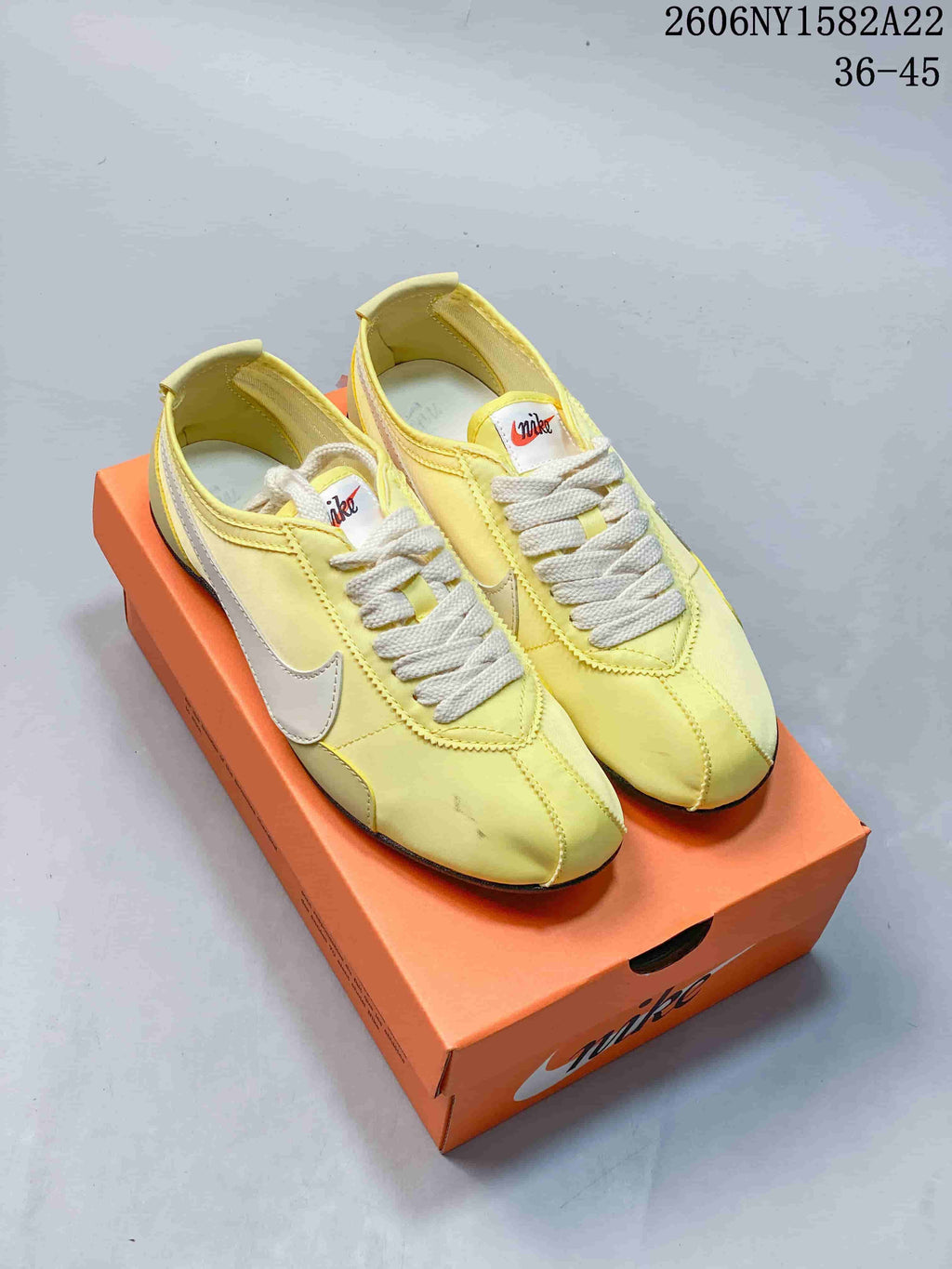 Pair of pale yellow Nike Moon Shoe OG low-top sneakers with cream laces and white Swoosh details on an orange box