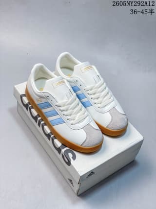Pair of white Adidas low-top sneakers with light blue stripes and gum-colored outsoles displayed on an Adidas shoebox.