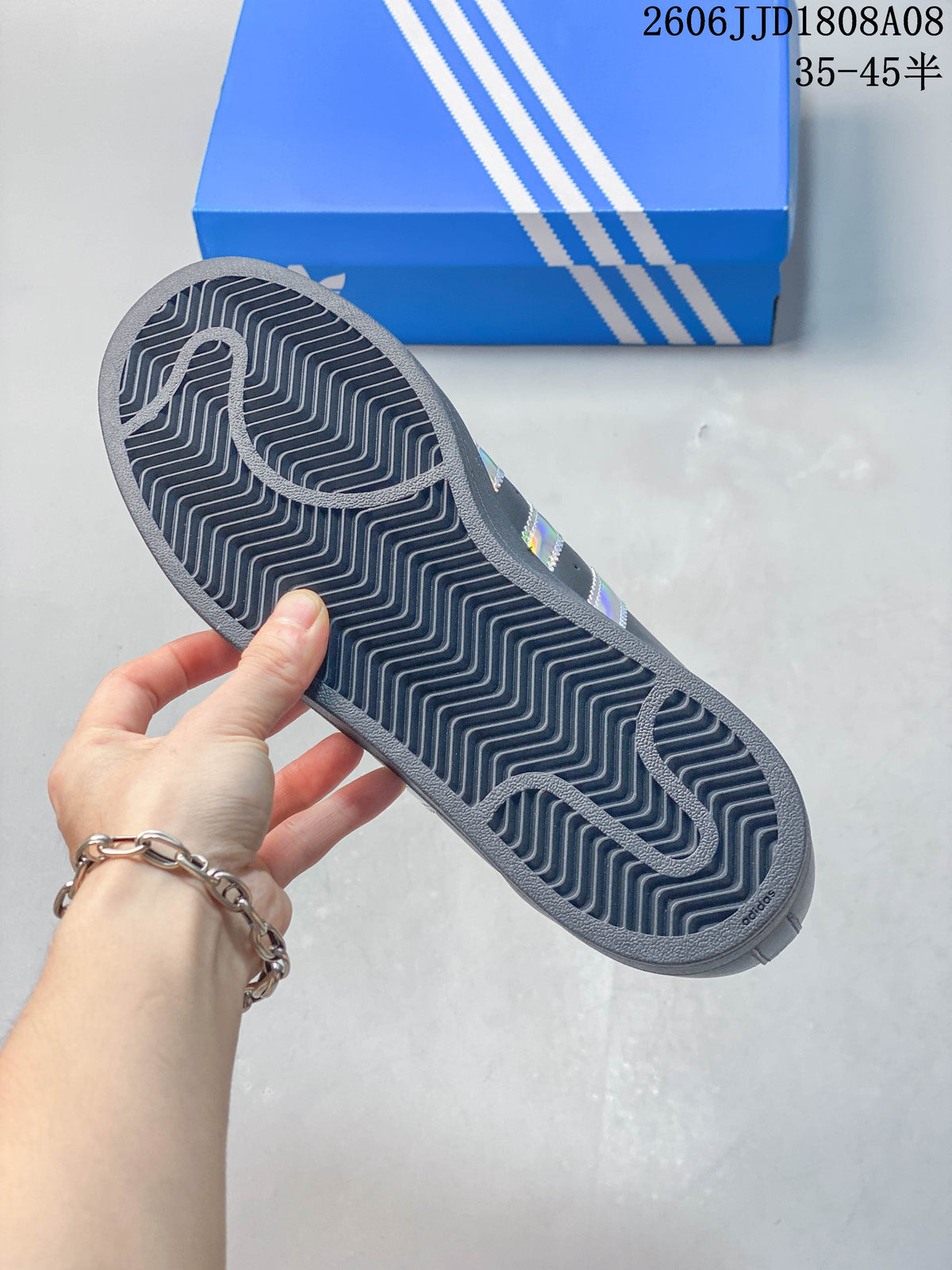 Outsole view of a charcoal Adidas Superstar sneaker with a patterned tread.