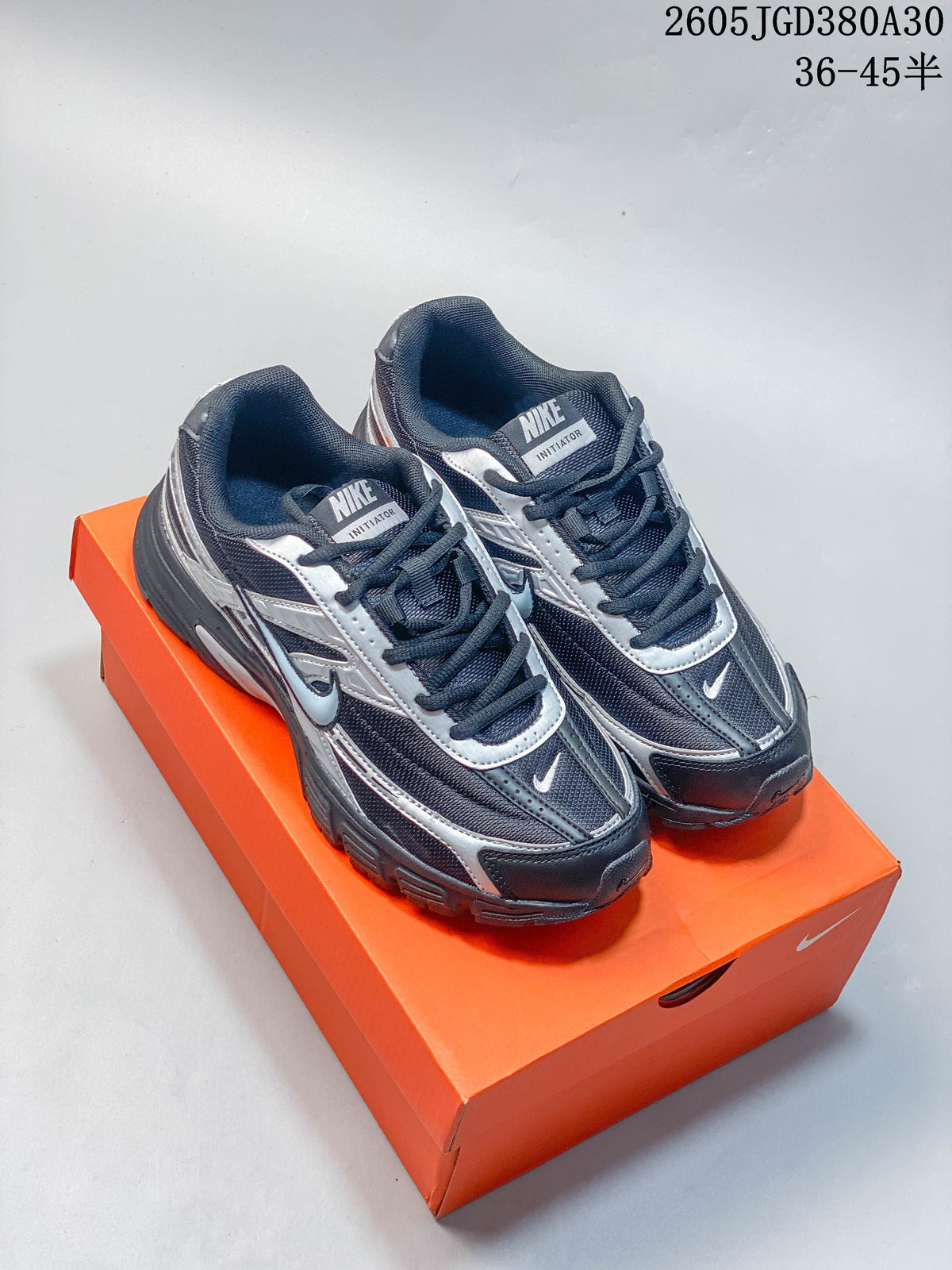 Pair of charcoal and silver Nike Initiator sneakers on an orange box
