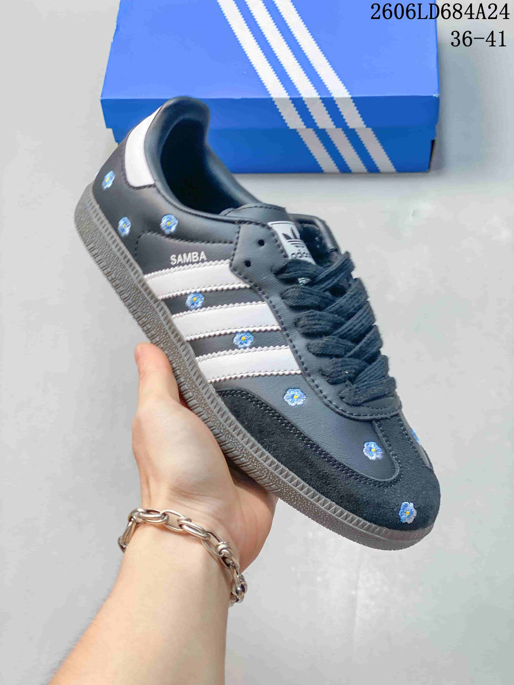 Close-up of a charcoal Adidas Samba sneaker with blue flower motifs and white stripes.