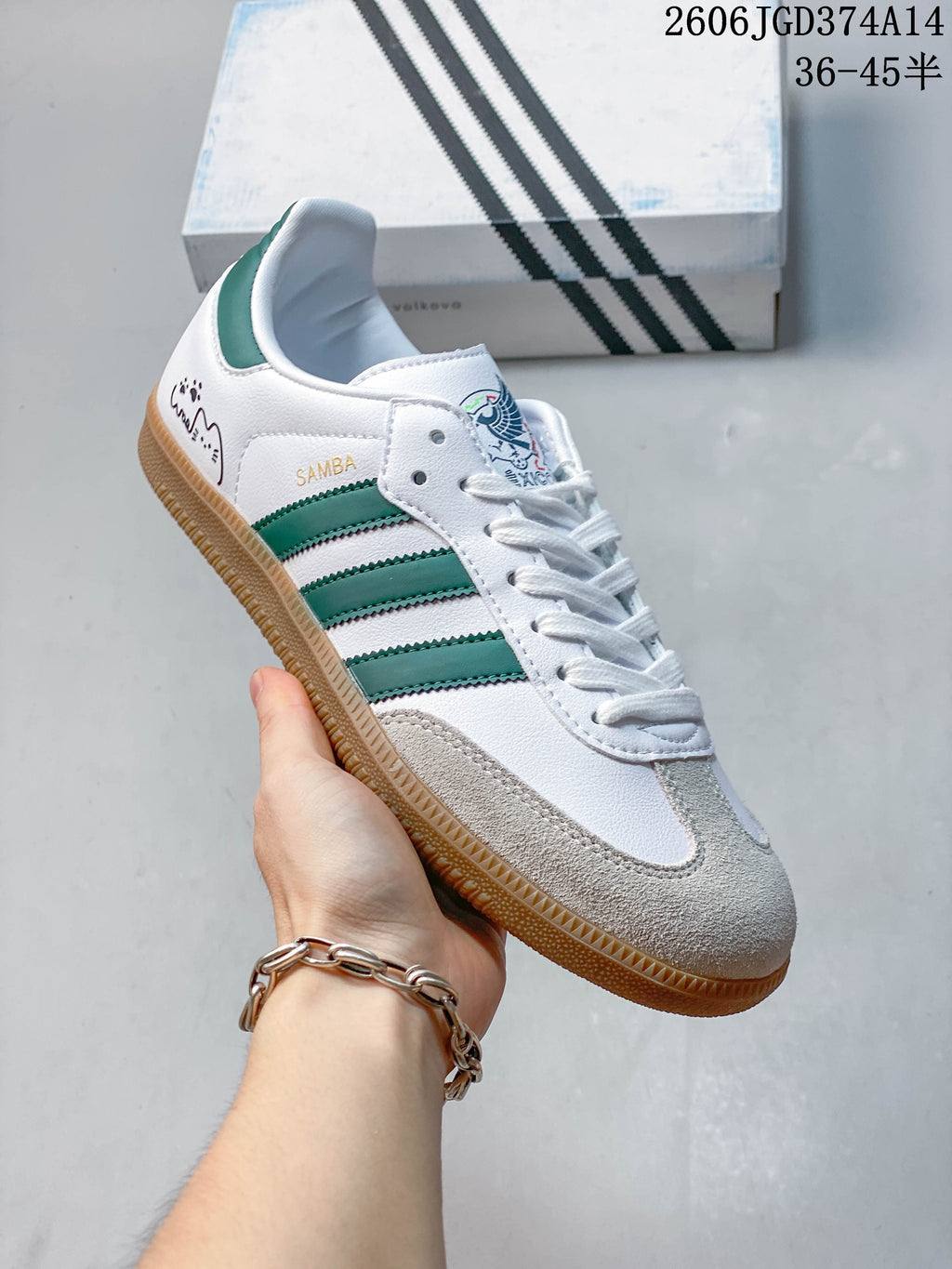 White Adidas Samba-style sneaker with green stripes, a gum sole, and decorative heel graphics.