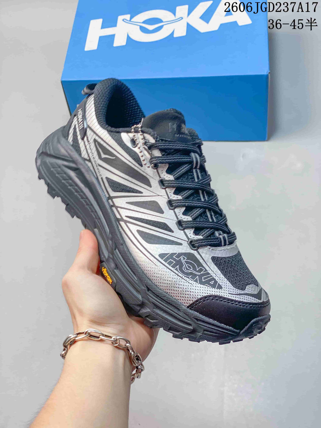 Angled side view of a silver-grey HOKA trail shoe with a rugged outsole