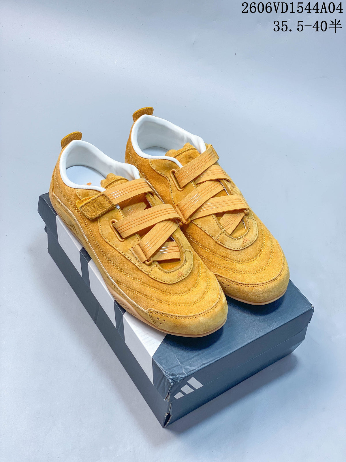 Pair of golden yellow Adidas Urban Reverie low-top sneakers with strap-and-lace closures, shown on a shoe box.