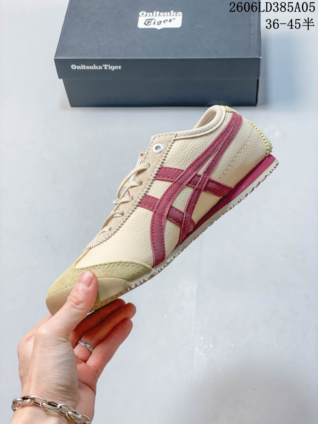 Side profile of a beige sneaker with burgundy stripes and a contrasting toe overlay
