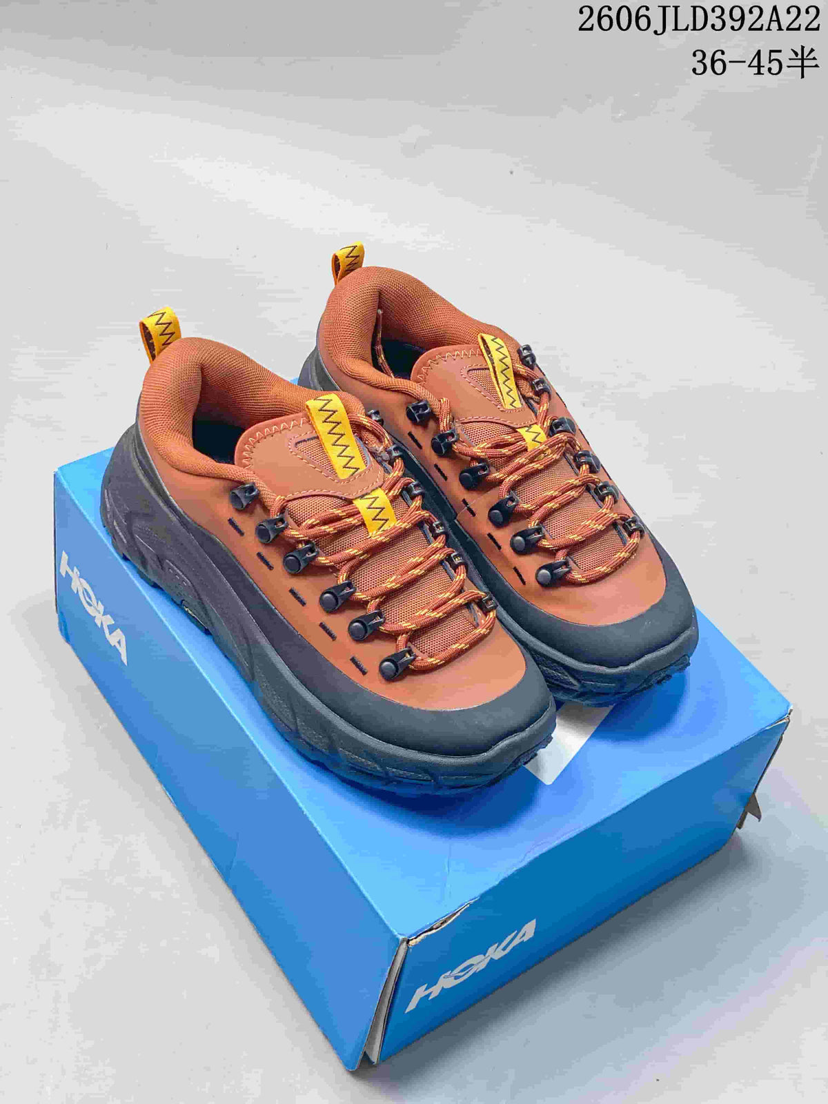 Pair of rust-orange and charcoal HOKA Tor Summit low-top shoes on a blue box