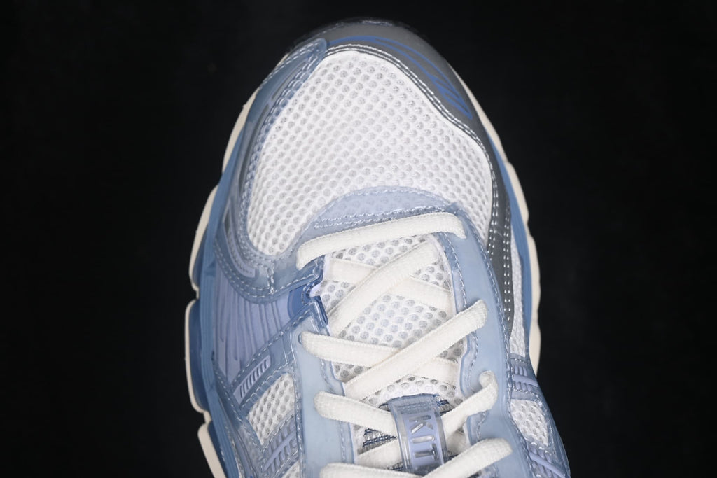 Close-up of the cream and light blue ASICS sneaker showing the mesh toe box, white laces, and layered blue overlays.