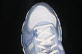Close-up of the cream and light blue ASICS sneaker showing the mesh toe box, white laces, and layered blue overlays.