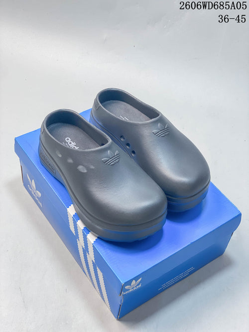 Pair of dark slate blue-gray Adidas AdiFOM Stan Smith mules on a blue shoe box