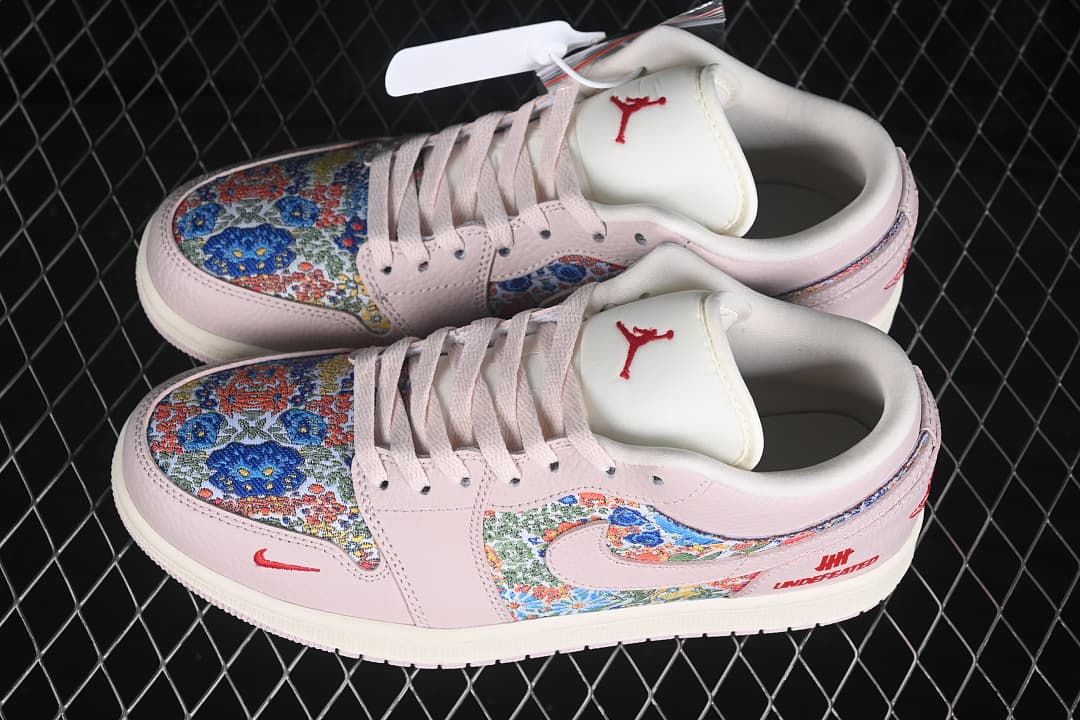 Pair of pale pink low-top sneakers with multicolor floral panels, red logo accents, and an off-white sole