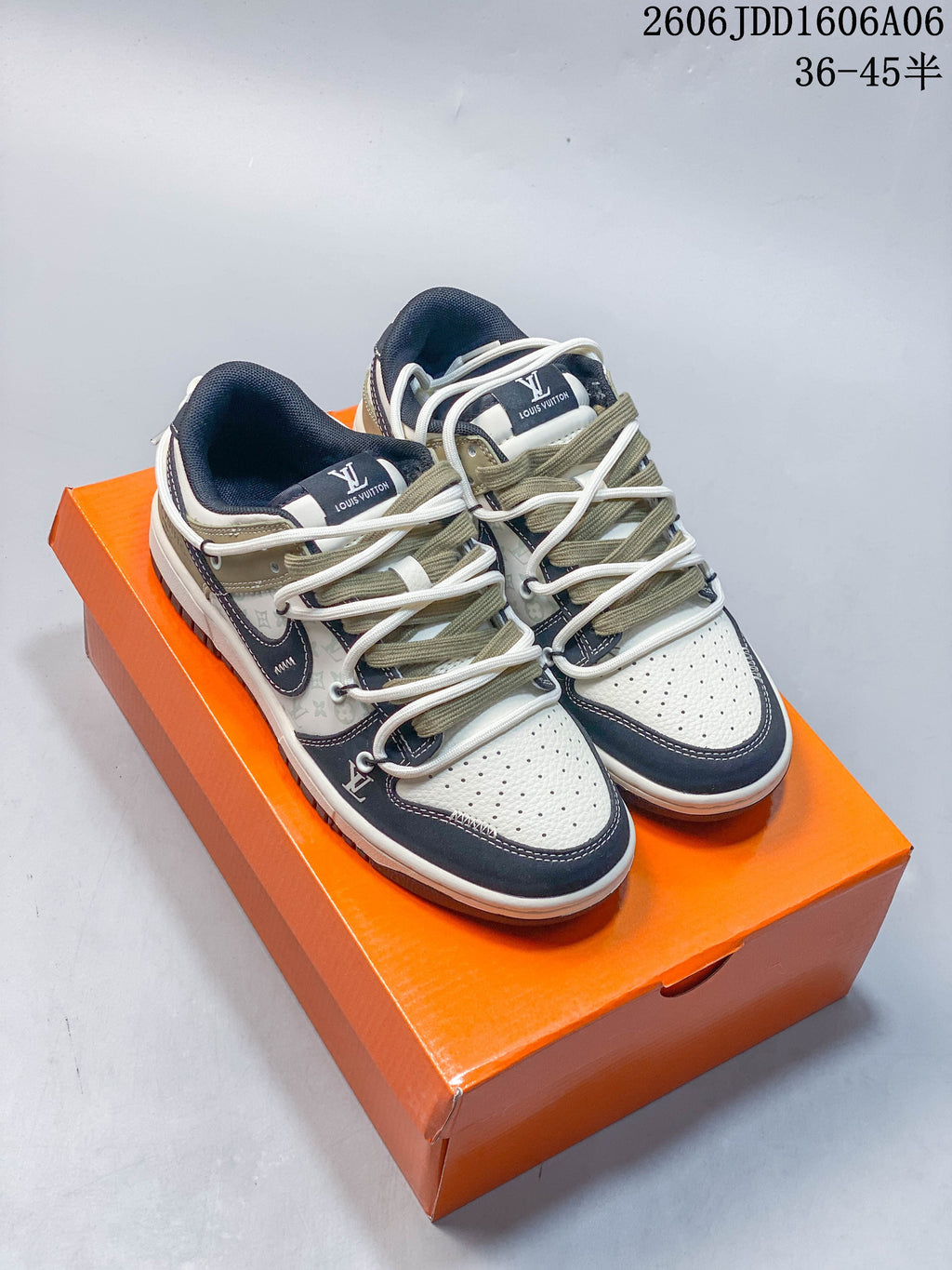 Pair of cream and navy Nike SB Dunk Low sneakers with layered laces, shown on an orange box