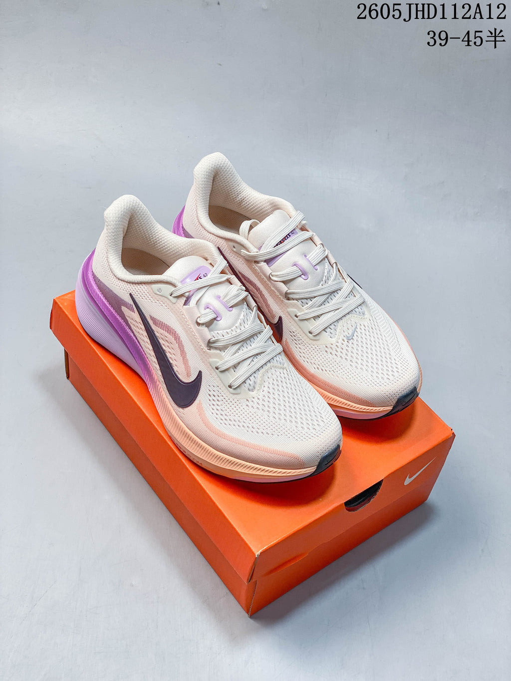 Pair of cream Nike Air Zoom Pegasus 42 running shoes with peach and purple accents on an orange shoe box.