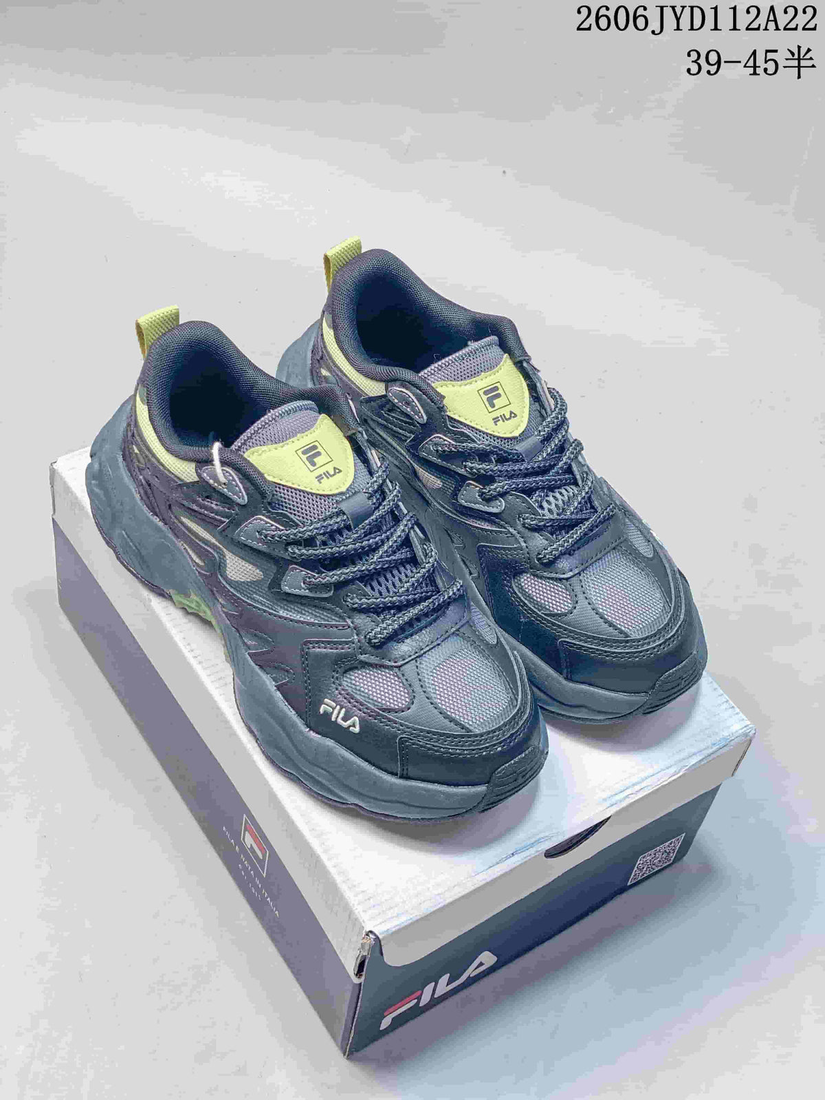 Pair of charcoal-gray FILA sneakers with lime accents shown on a shoebox