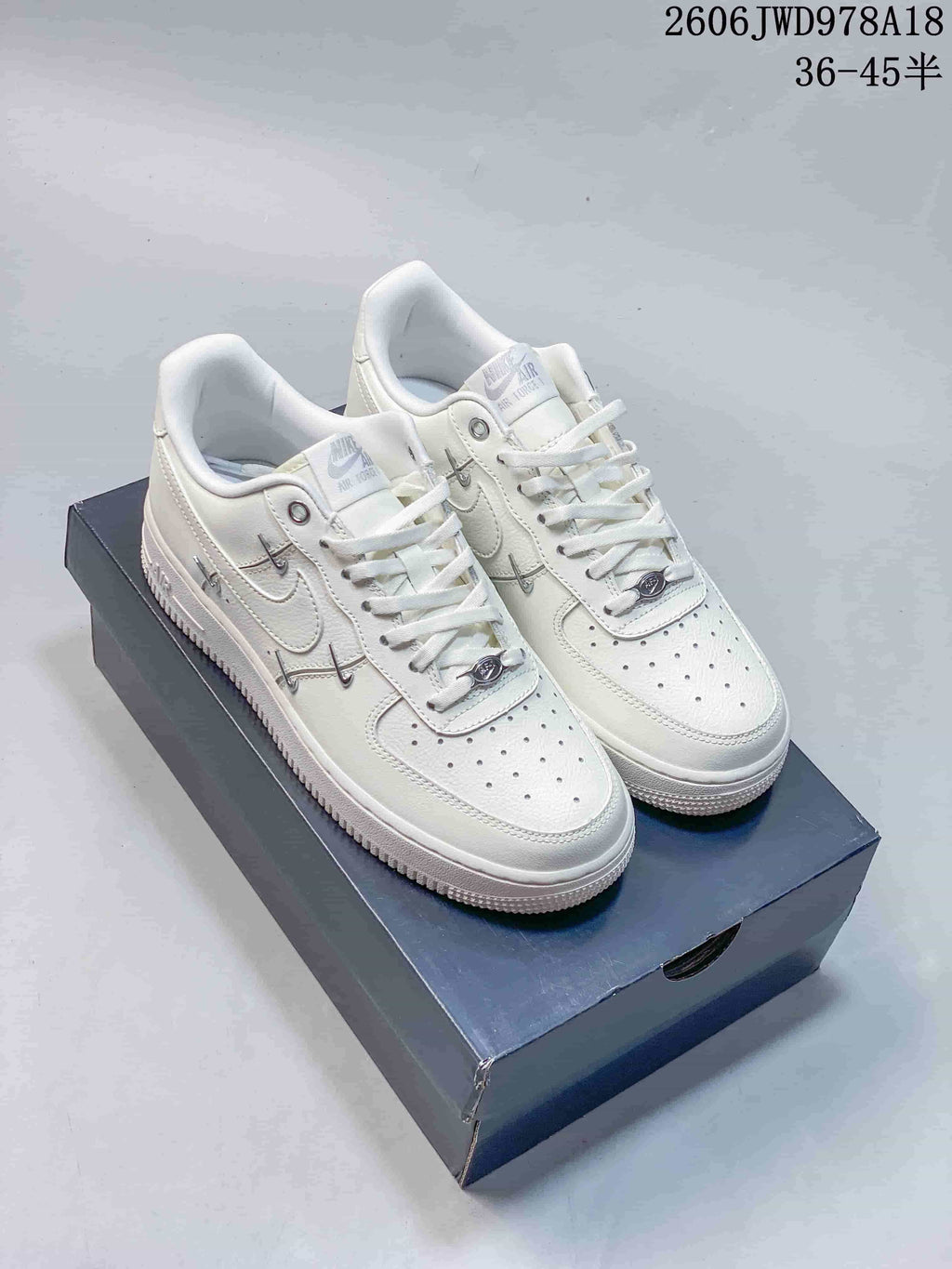 Pair of white Nike Air Force 1 low-top sneakers with metallic side and lace accents, shown on a box.