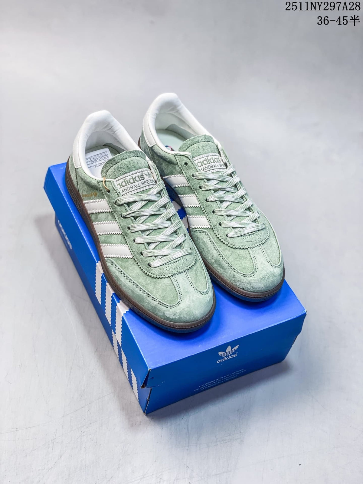 Pair of pale green adidas Handball Spezial sneakers with white stripes and brown outsoles, shown on a blue shoebox.